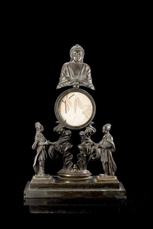 Portaorologio in bronzo brunito sovrastato da figura del Buddha in...