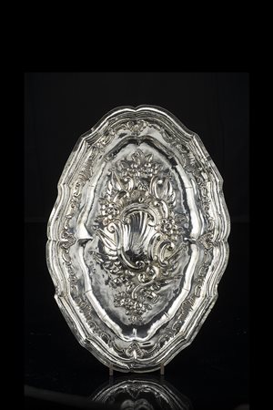 Piatto da parata in argento di forma ovale mistilinea, sbalzato e cesellato...
