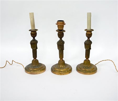 Gruppo di tre candelieri ad una fiamma in bronzo dorato e cesellato a motivi...