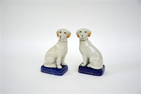 Coppia di sculture in porcellana raffiguranti cani assisi decorati in policromia