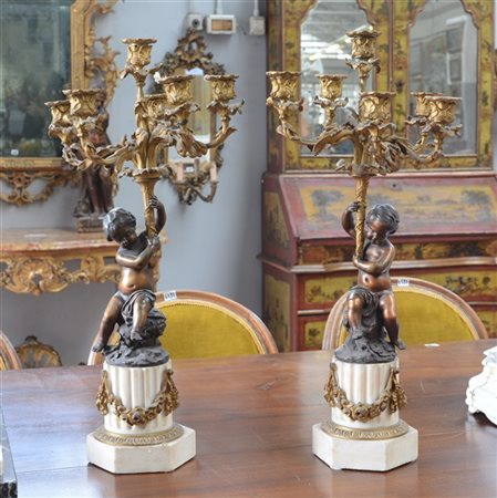 Coppia di candelabri in bronzo a sei braccia fogliate retti da amorini assisi p