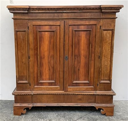 Antica credenza a due ante riquadrate, fascia superiore con profili intagliati,