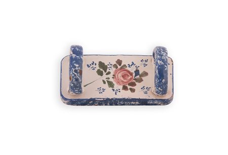 Manifattura castellana del XIX secolo ( - ) 
Schiacciapatate in maiolica policroma. Al centro su fondo bianco decorato con una rosa. Sul doppio manico e sul perimetro motivo in blu realizzato a spugnetta.  
 cm 8x23x10