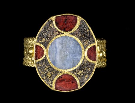 A LARGE SAXON GOLD RING WITH BREADED SHANK AND BLUE CHALCEDONY, GARNETS AND GLASS PASTE ON THE BEZEL. 