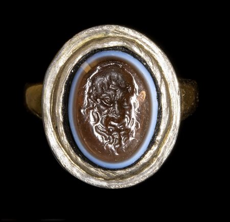 A GLASS IMPRESSION SET IN A GOLD RING. MASK OF A FAUN.