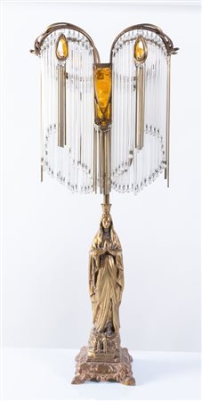 Lampada da tavolo in bronzo raffigurante Notre Dame de Lourdes sormontata da paralume di frange di canottiglie, perline di vetro e vetro incolore e colore ambra. Francia, XX secolo. Cm 73x30x19.