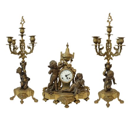 Trittico composto da orologio da tavolo in bronzo patinato oro con putti ai lati, quadrante in porcellana firmato Imperial e coppia di candelieri in bronzo patinato oro a cinque luci retti da basi con putti