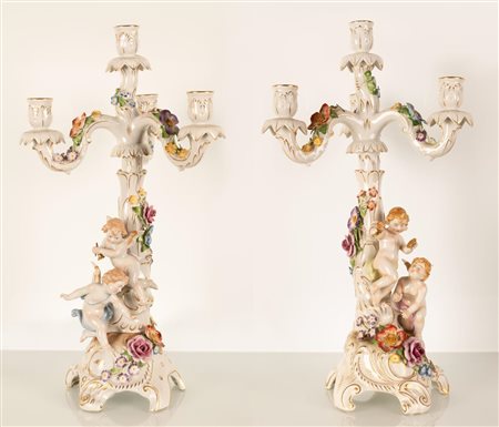 Coppia di grandi candelieri in porcellana con decoro plastico formato da putti e ghirlande di fiori a rilievo disposti sulla base e sugli elementi decorativi dei bracci (in stile rococò)  Manifattura Sitzendorf, inizi del XX secolo.    