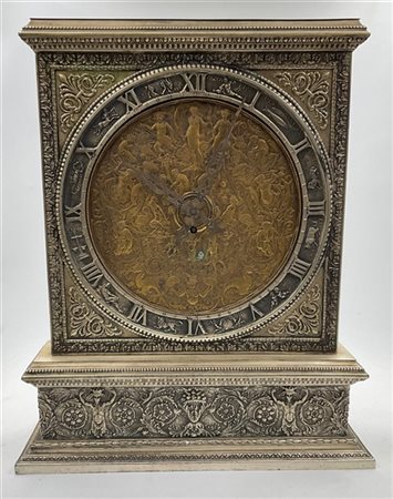 Orologio in metallo argentato e ottone. Mostra riccamente decorata a bassorilie