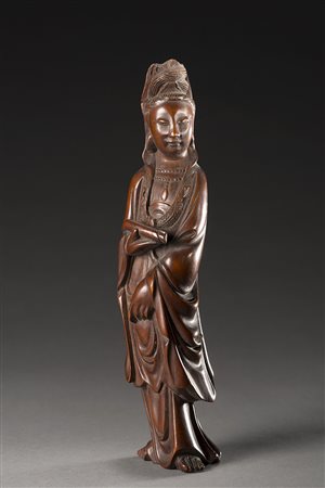 Guanyin in legno scuro, con capelli raccolti, lunga veste che si apre sul...