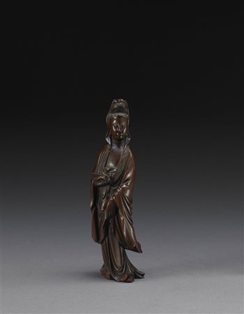 Guanyin in legno intagliato, raffigurata in piedi con espressione serena,...