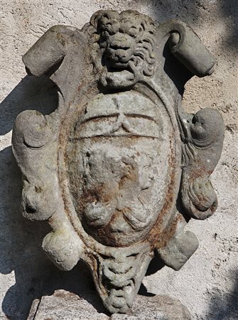 Stemma nobiliare in pietra decorato a volute, testa leonina e Giano bifronte....